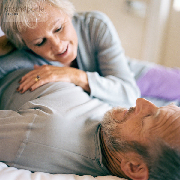 Seniorenpaar liegend  Frau auf dem Bauch des Mannes lehnend