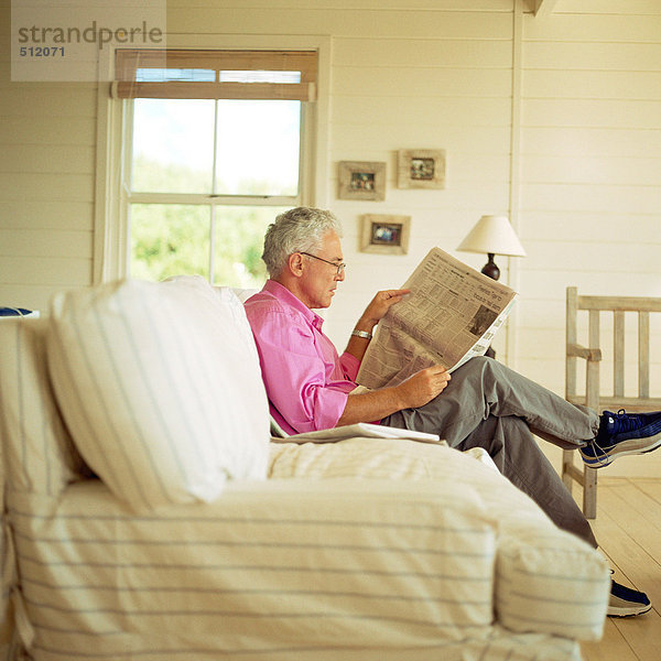 Erwachsener Mann sitzt auf dem Sofa  liest Zeitung  Seitenansicht