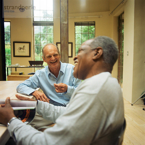 Zwei reife Männer sitzen am Tisch und lachen.