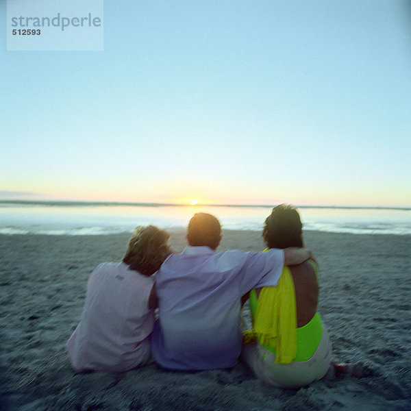 Reife Freunde sitzen am Strand  Rückansicht