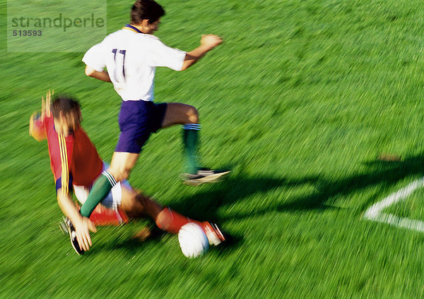 Fußballspieler greift nach dem Ball  Gegner springt über das Bein  verschwommen.