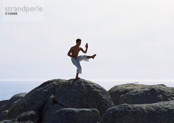 Mann  der Tai Chi auf einem Felsen am Meer macht.