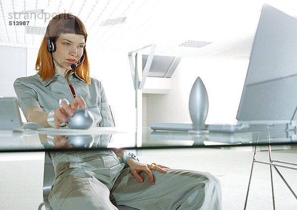 Frau mit Headset  am Schreibtisch sitzend  dreiviertel Länge