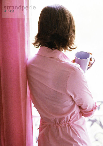 Frau hält Tasse  Blick aus dem Fenster  Rückansicht