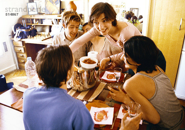 Vier Leute sitzen am Tisch  eine Frau bringt den Teller.