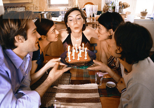 Vier Leute halten Kuchen  eine Frau bläst Kerzen aus.