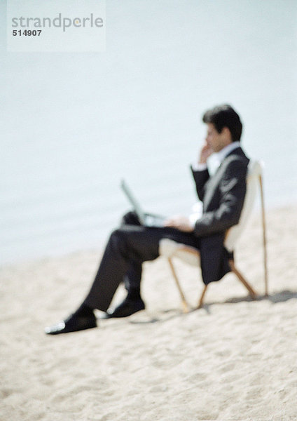 Geschäftsmann am Strand sitzend mit Laptop auf Knien  durchgehend  Nahaufnahme  verschwommen
