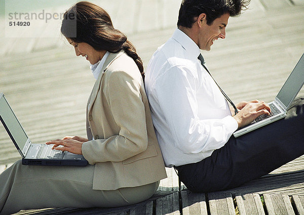 Geschäftsmann und Frau Rücken an Rücken auf dem Boden mit Laptop-Computern auf dem Schoß