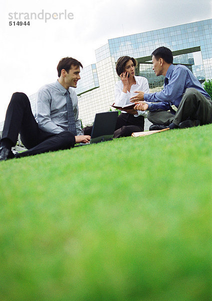 Drei Personen sitzen auf Gras  bauen im Hintergrund