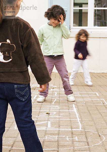 Drei Kinder spielen Hopscotch