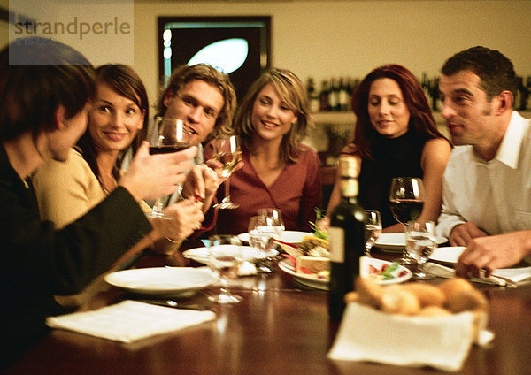 Gruppe junger Leute  die am Tisch sitzen und gemeinsam zu Abend essen.