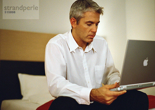 Geschäftsmann auf dem Bett sitzend mit Laptop
