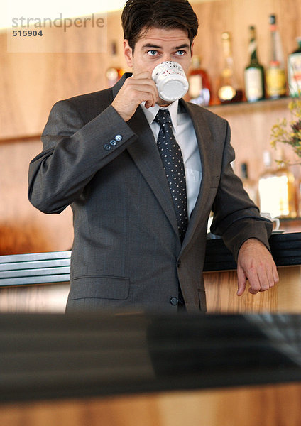 Geschäftsmann steht an der Bar und trinkt aus der Kaffeetasse.