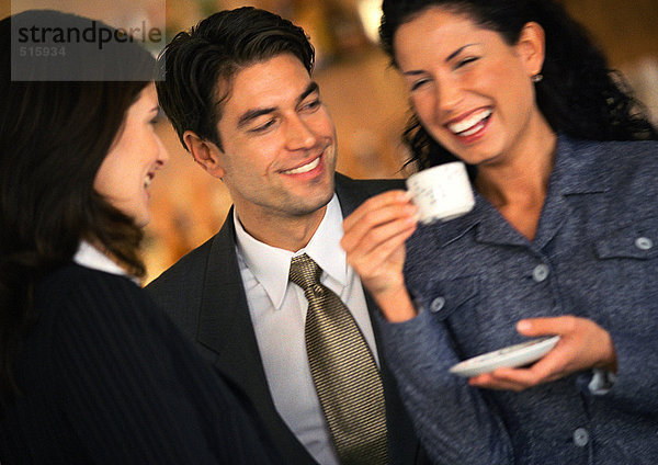 Geschäftsmann und Geschäftsfrau beobachten zweite Geschäftsfrau beim Kaffeetrinken  Lachen