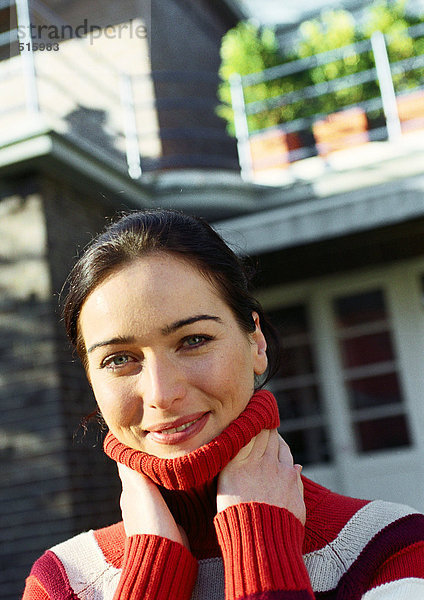 Junge Frau vor dem Haus mit Händen am Hals  lächelnd vor der Kamera