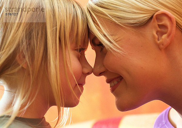 Junge Frau und kleines Mädchen lächelnd mit berührenden Stirnen und Nasen  Seitenansicht  Nahaufnahme  Kopfschuss