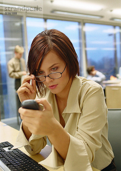 Geschäftsfrau  die eine Brille anpasst und auf das Telefon schaut  im Büro  Nahaufnahme.