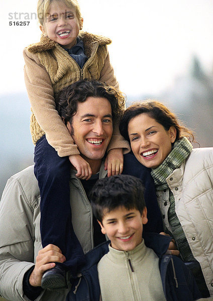 Erwachsener Mann und Frau stehend mit zwei Kindern  kleines Mädchen auf den Schultern des Mannes  kleiner Junge vorne stehend  Porträt