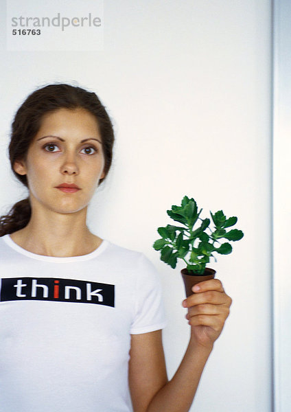 Porträt einer Frau  die eine kleine Topfpflanze mit der Hand hochhält.
