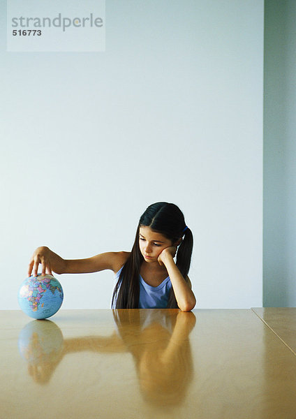 Mädchen am Tisch sitzend mit der Hand auf dem Globus