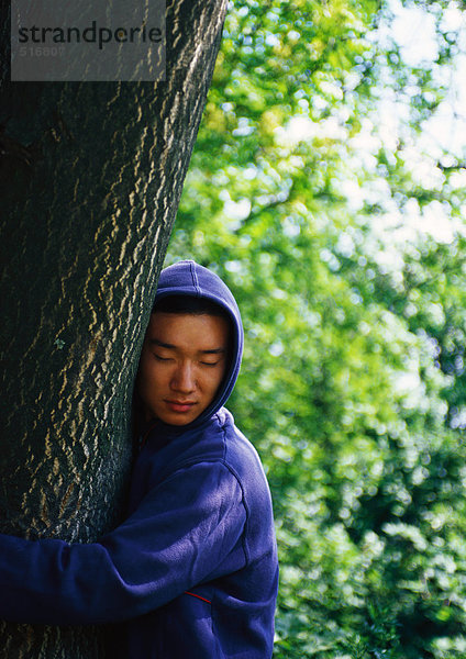 Mann mit Kapuzenpulli umarmend Baum