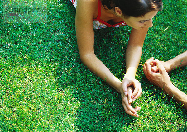 Frau auf dem Bauch auf Gras liegend  Hände zusammen  neben Männerhänden  Nahaufnahme