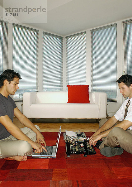 Mann mit Laptop und zweiter Mann mit Schreibmaschine  Seitenansicht