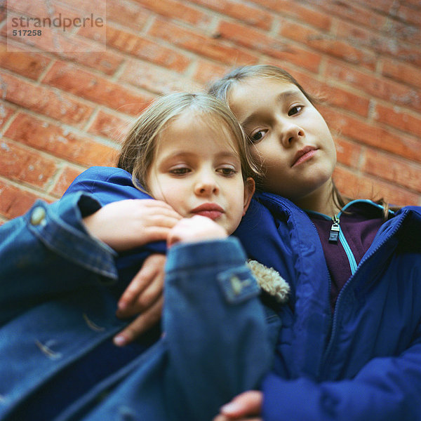 Zwei Mädchen  die sich umarmen  Backsteinmauer im Hintergrund  niedriger Blickwinkel