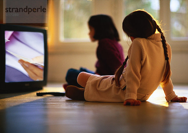 Junge Mädchen  die auf dem Holzboden sitzen und fernsehen  Mädchen im Hintergrund verschwommen