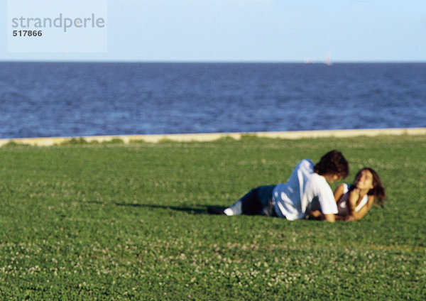 Junges Paar  zusammen auf Gras am Wasser liegend  verschwommen