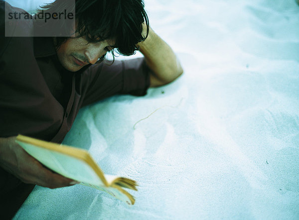 Mann auf Sand liegend  lesend  Nahaufnahme