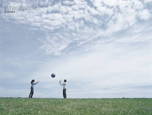 Junger Mann und Frau  die in der Ferne auf Gras stehen und den Ball werfen.