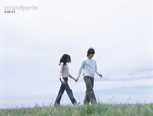 Junger Mann und Frau  die auf Gras gehen und Hände halten.