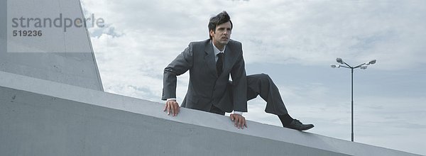 Mann im Anzug klettert über niedrige Betonwände