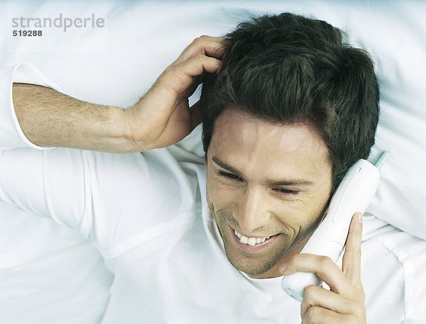 Mann im Bett liegend  schnurloses Telefon am Ohr haltend  lächelnd