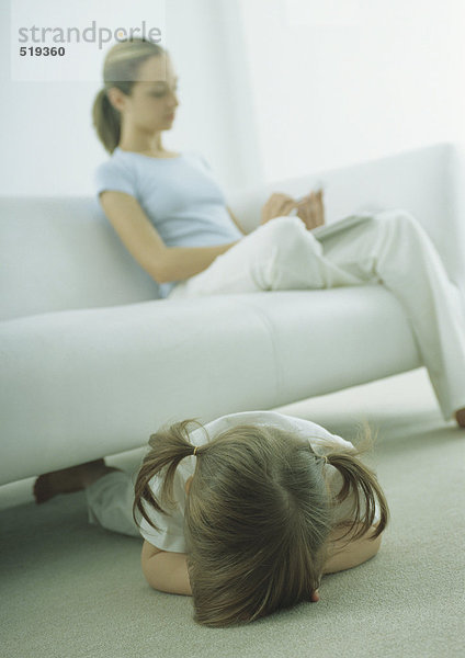 Kleines Mädchen auf dem Boden liegend  junge Frau auf dem Sofa sitzend  lesend