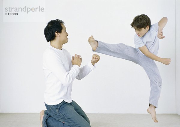 Junge gibt Karate Kick in der Luft  Mann auf Knien mit ausgestreckten Fäusten