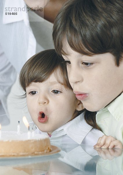 Junge und kleines Mädchen blasen Kerzen auf Kuchen aus  Mutter im Hintergrund