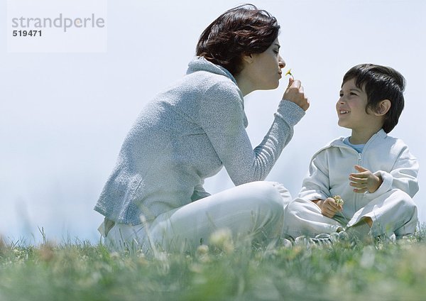 Frau und Sohn sitzen auf Gras  Frau riecht Blume