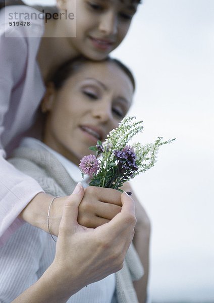 Mädchen umarmt Mutter von hinten  Mutterhand über Mädchen  mit Blumenstrauß