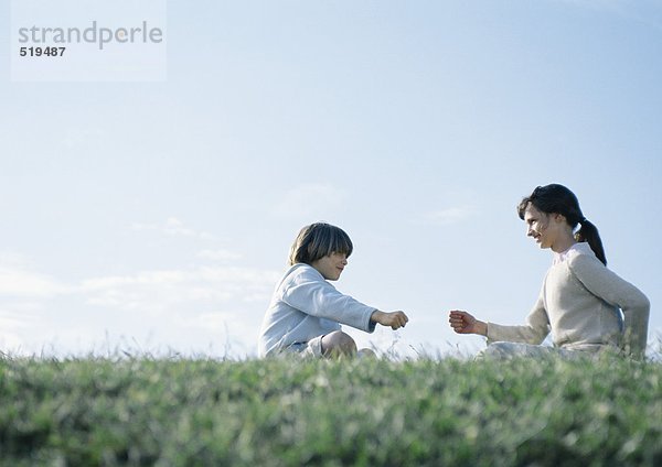 Junge und Mädchen sitzen auf Gras und spielen eine Steinschere.