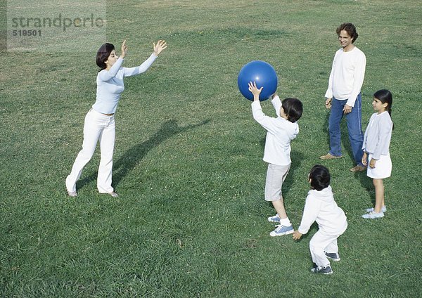 Eltern mit Jungen und Mädchen beim Ballspielen auf Rasen  volle Länge