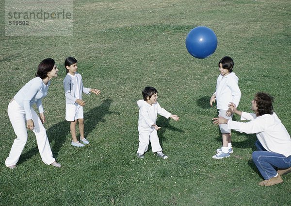Eltern mit Jungen und Mädchen beim Ballspielen auf Rasen  volle Länge