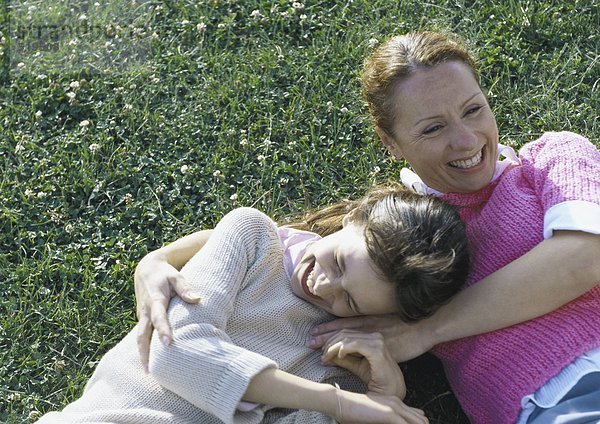 Frau und Tochter lachend auf Gras liegend