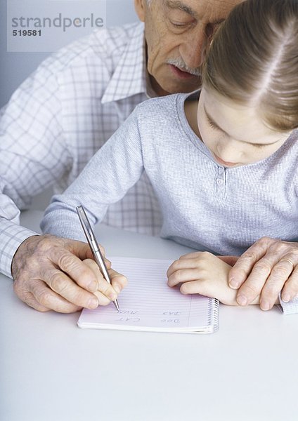 Großvater hilft Enkelin schreiben in Notizbuch