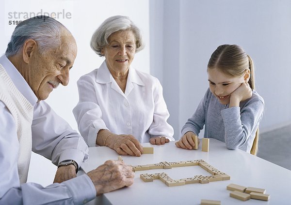 Großeltern und Mädchen am Tisch beim Domino spielen