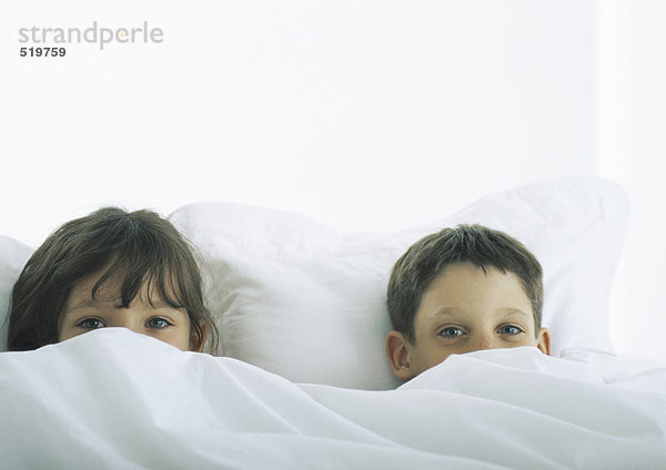 Junge und Mädchen im Bett liegend  Gesichter teilweise mit Bettdecke bedeckt