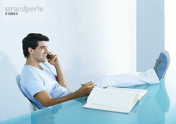 Mann am Tisch sitzend mit erhobenen Füßen  telefonierend