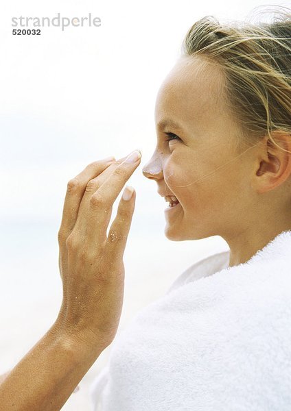 Kleines Mädchen in Handtuch gewickelt mit Sonnencreme  die von Mutter in die Nase gerieben wurde.