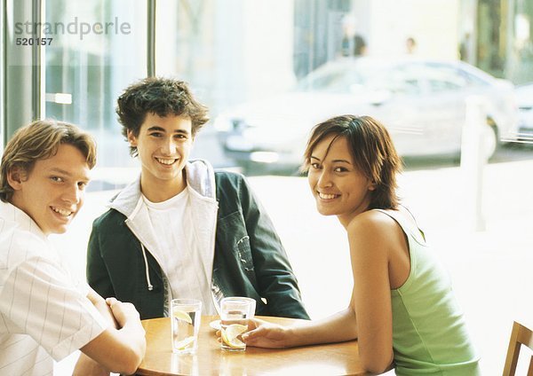 Gruppe junger Leute sitzt am Tisch im Café und lächelt vor der Kamera.